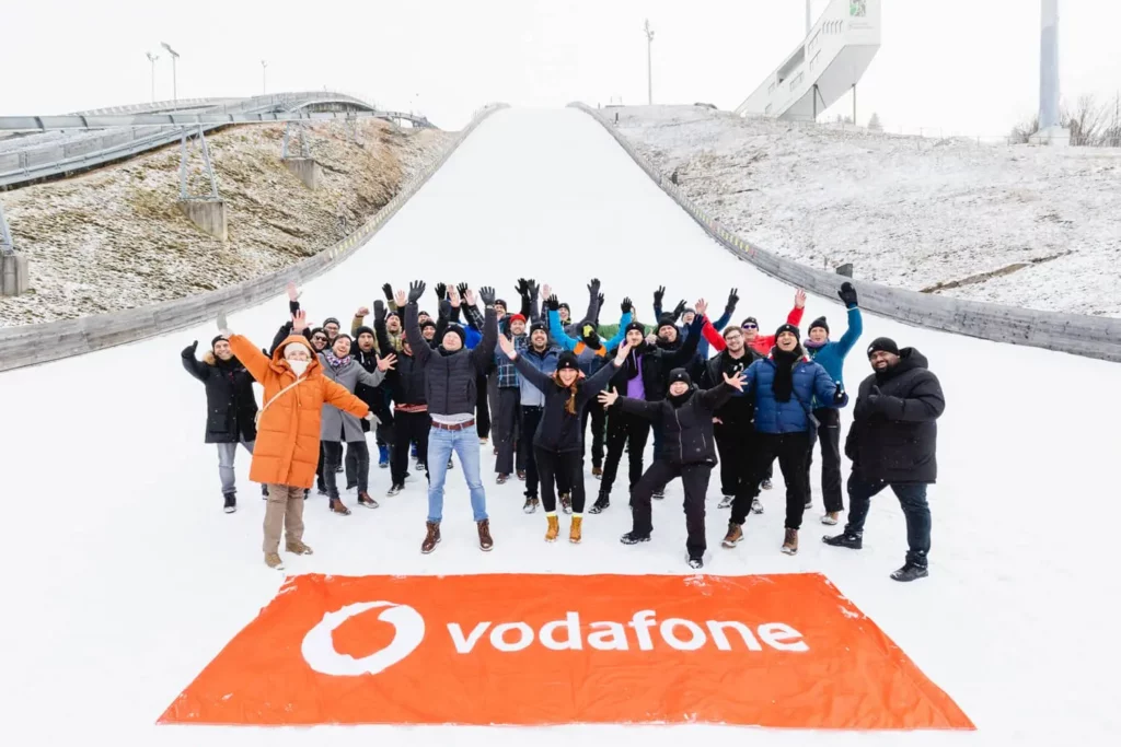Gruppe von Menschen jubelt auf schneebedecktem Hügel, Vodafone-Banner im Vordergrund