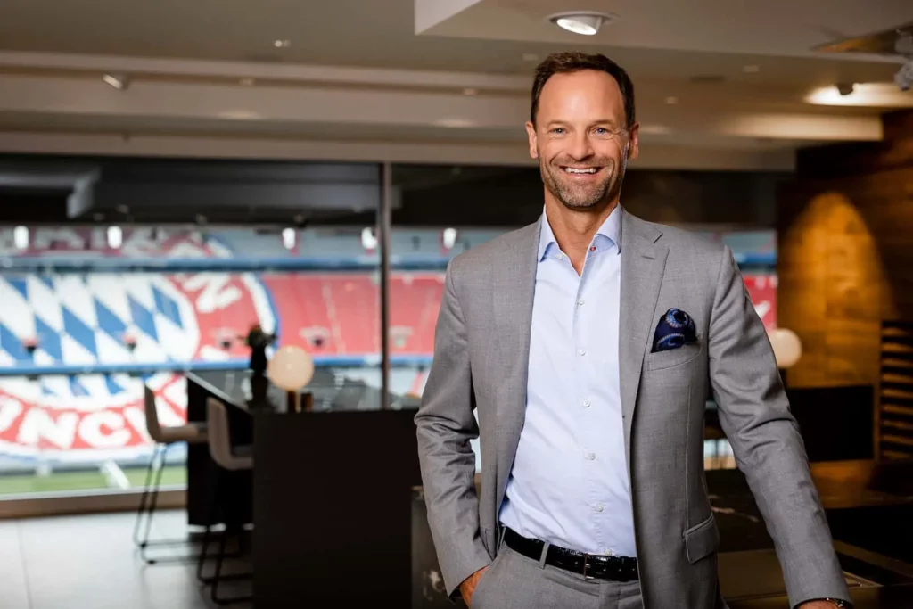 Lächelnder Mann im Anzug im Büro mit Stadionblick in München
