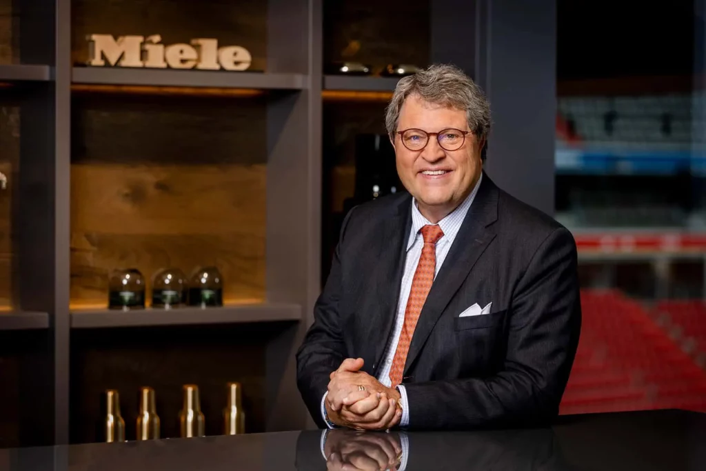 Mann in Anzug vor Miele-Logo in modernem Büro