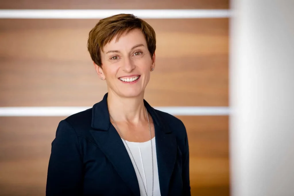 Frau mit kurzem Haar in Businesskleidung vor Holzwand