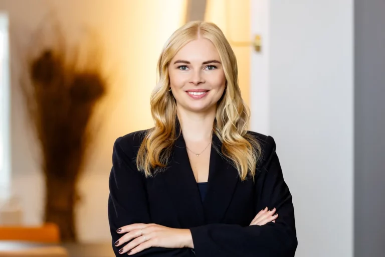 Porträt einer lächelnden Frau in professioneller Kleidung vor neutralem Hintergrund