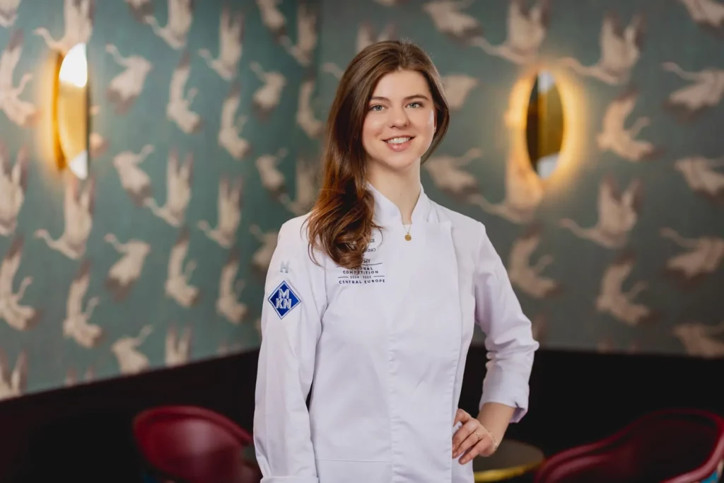 Junge Köchin in weißer Uniform vor dekorativer Tapete