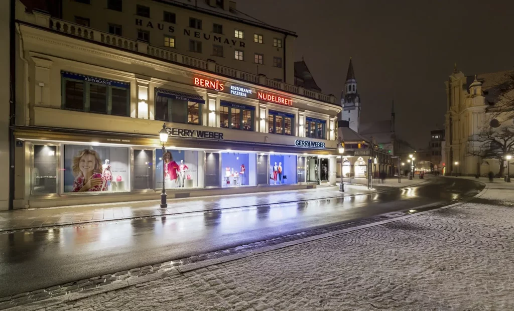Nächtliche Ansicht einer Einkaufsstraße mit beleuchteten Geschäften in München
