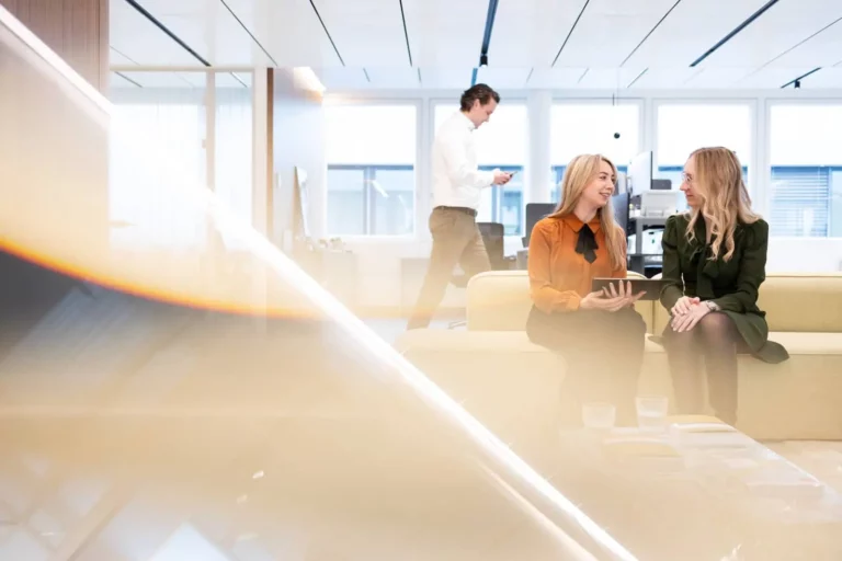 Kollegen im modernen Büro, zwei Frauen im Gespräch, Mann im Hintergrund