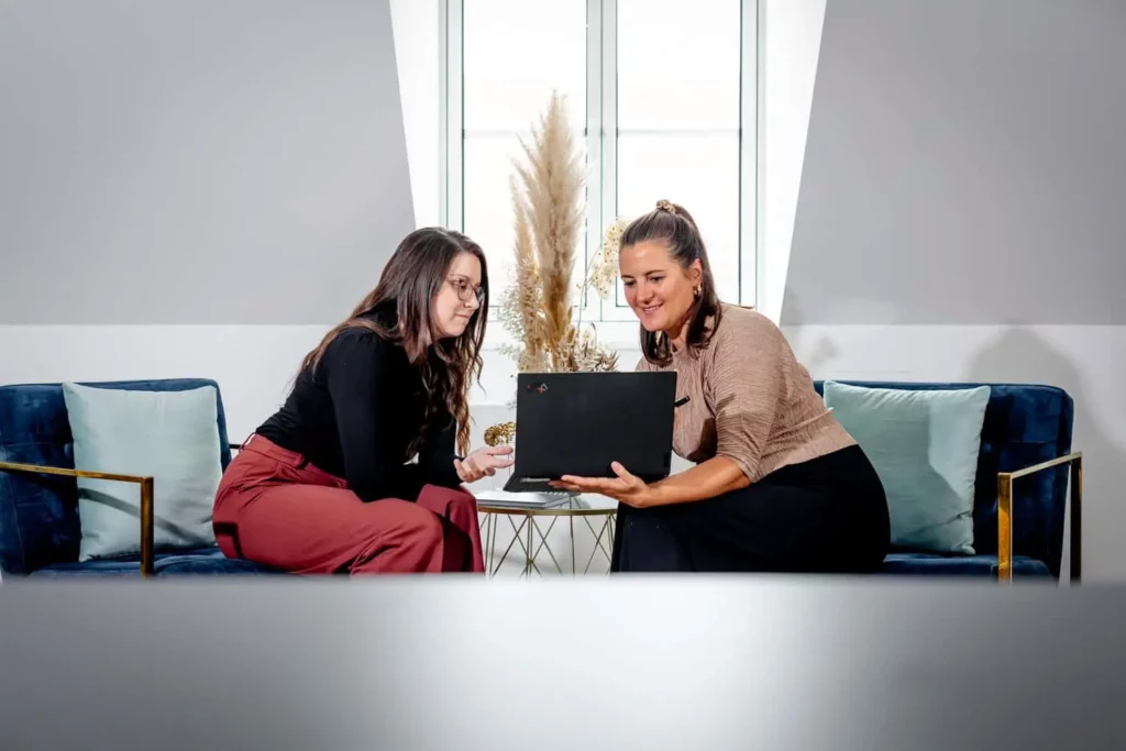 Zwei Frauen arbeiten zusammen an einem Laptop in einem modernen Büro