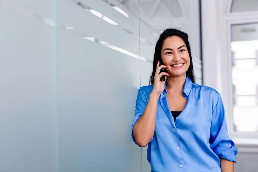Lächelnde Frau in blauem Hemd telefoniert im modernen Büro