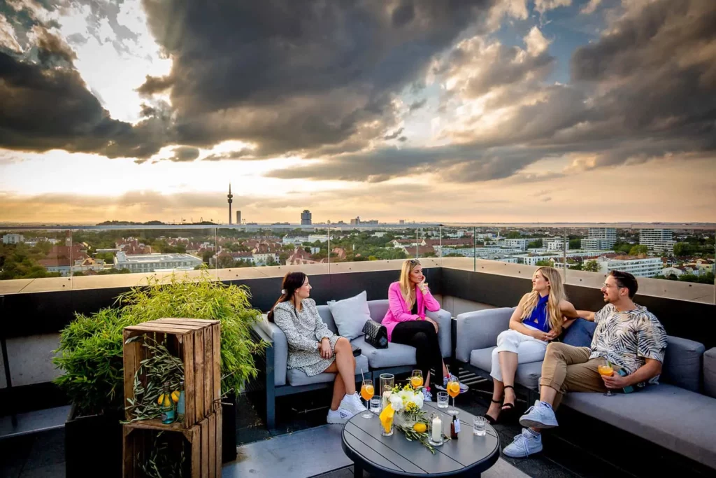 Personen genießen auf einer Dachterrasse bei Sonnenuntergang Getränke und Unterhaltung
