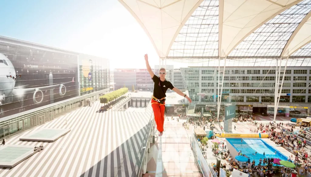 Seiltänzer balanciert auf Slackline im modernen Stadtdach mit Menschenmenge