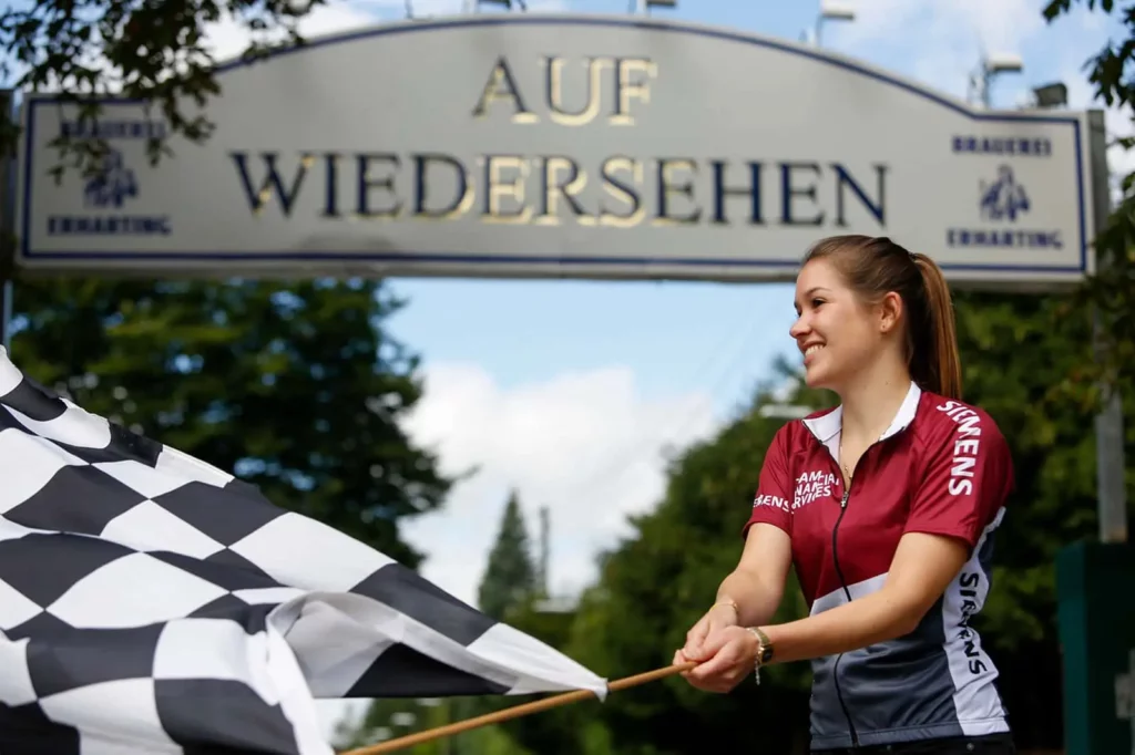 Frau schwenkt karierte Flagge vor Auf Wiedersehen Schild