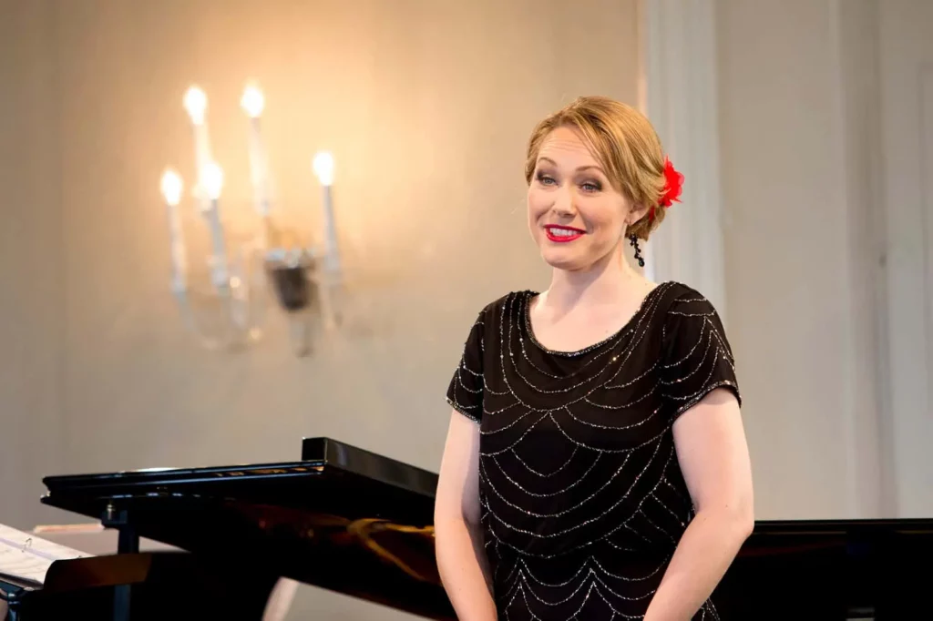 Frau in schwarzem Kleid steht vor einem Flügel im eleganten Raum