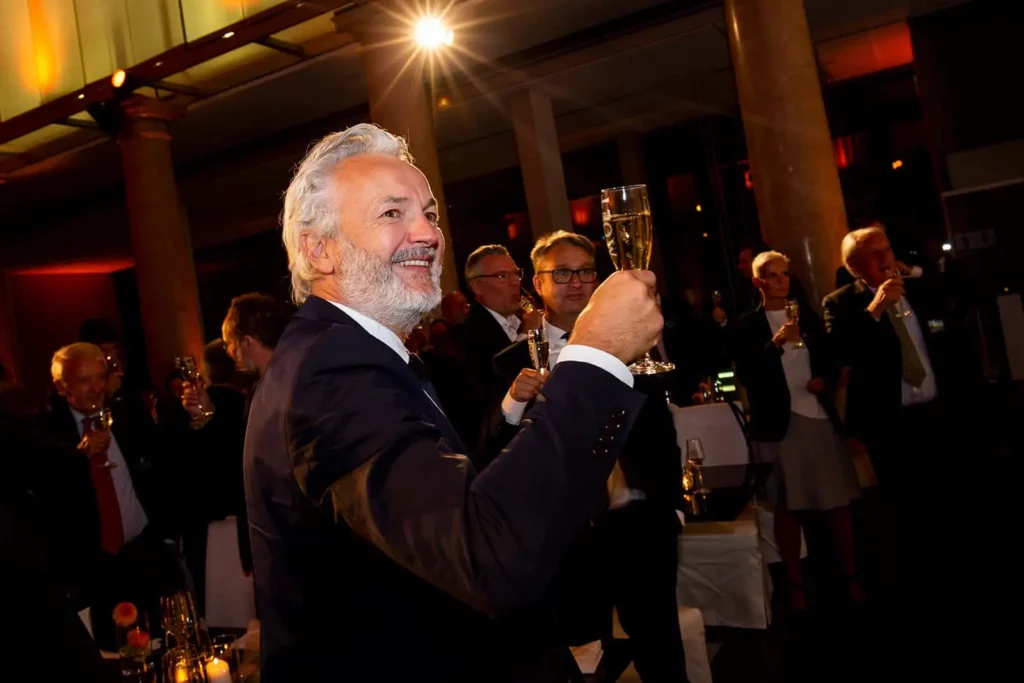 Älterer Mann hebt Glas bei eleganter Feier