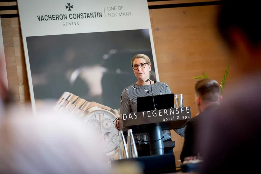 Frau hält Rede im Das Tegernsee Hotel vor Vacheron Constantin Plakat