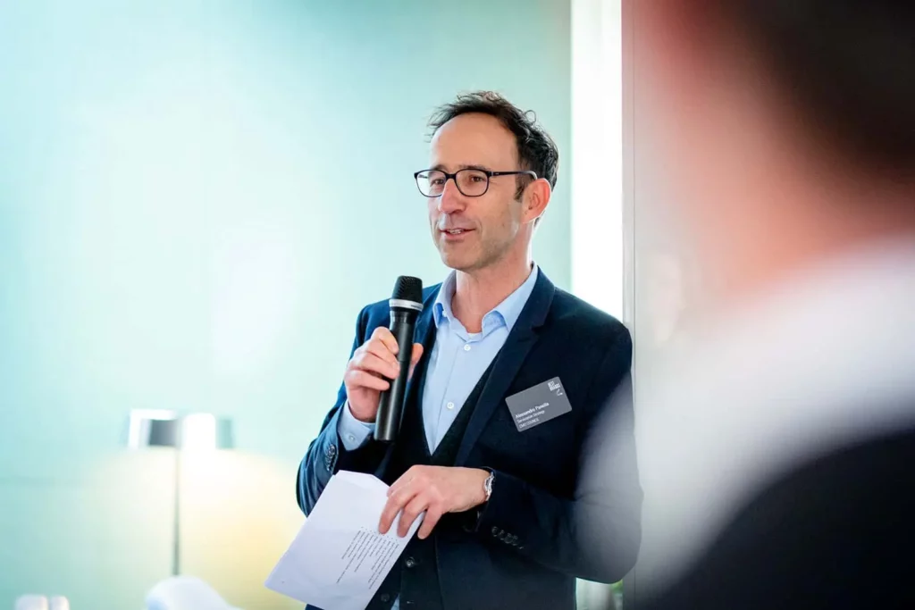 Mann hält Mikrofon und Präsentationsunterlagen bei einer Konferenz