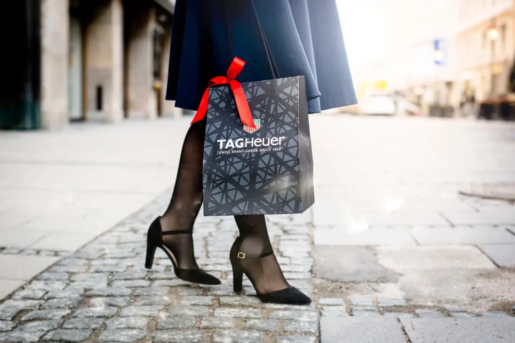 Frau trägt TAG Heuer Einkaufstasche auf Kopfsteinpflaster