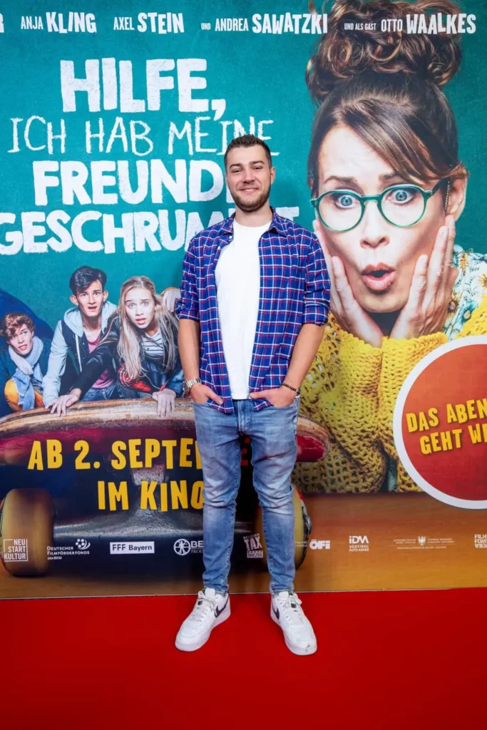 Mann auf rotem Teppich vor Filmplakat der Komödie 'Hilfe, ich hab meine Freunde geschrumpft'