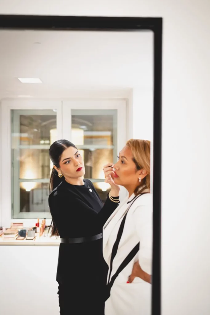 Visagistin schminkt Kundin in modernem Studio vor einem großen Fenster