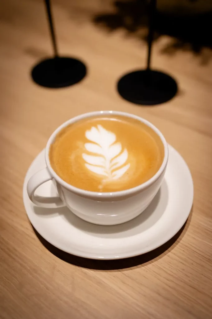 Kaffee mit Latte Art Blattmuster in weißer Tasse auf Holztisch