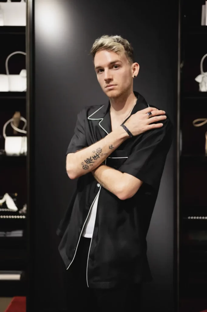 Mann in schwarzem Hemd posiert vor einem Regal mit Handtaschen