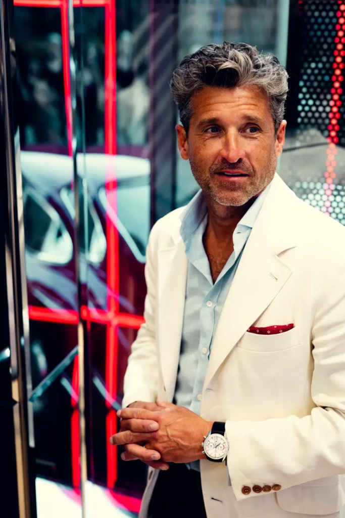 Mann im weißen Anzug mit Bart vor rotem Hintergrund