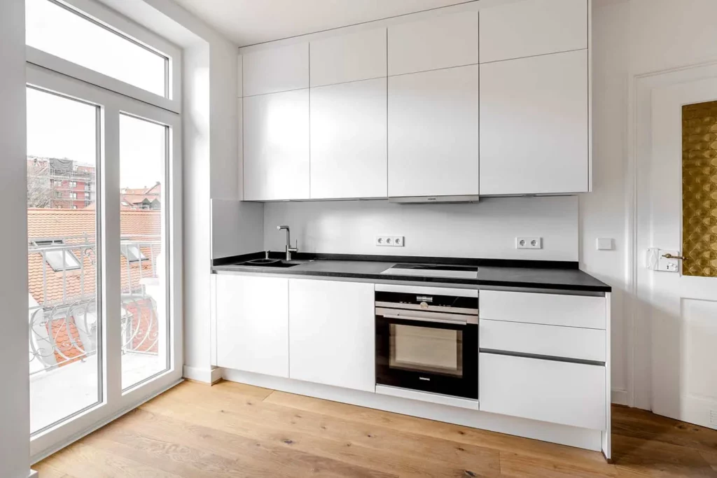 Moderne weiße Küchenzeile mit Holzfußboden und großen Fenstern