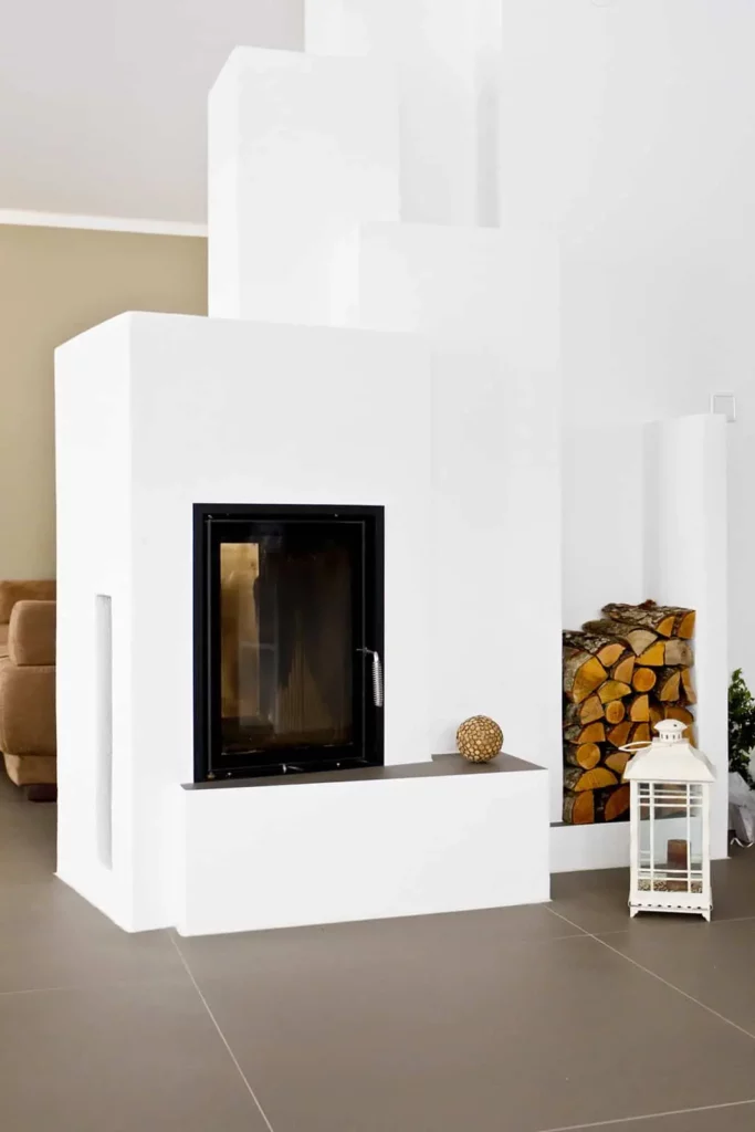 Moderner weißer Kamin mit Holzbeige und Sofa im Hintergrund