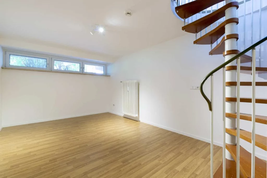 Leerer Raum mit Holztreppe und großen Fenstern