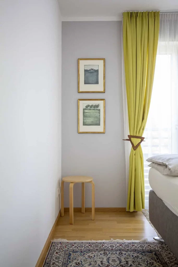 Minimalistisches Schlafzimmer mit gelben Vorhängen und schlichter Holzhocker
