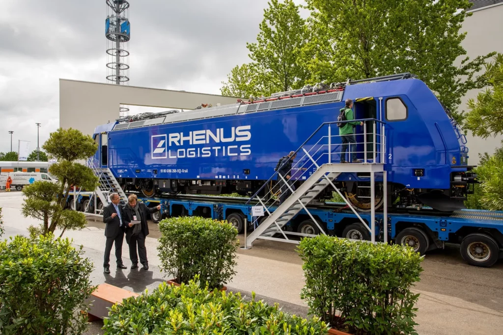 Blauer Lokomotiv-Transport von Rhenus Logistics auf einem LKW in städtischer Umgebung