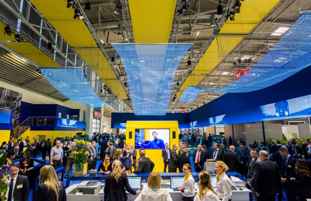 Menschenmenge auf lebhaftem Messegelände mit blau-gelber Dekoration