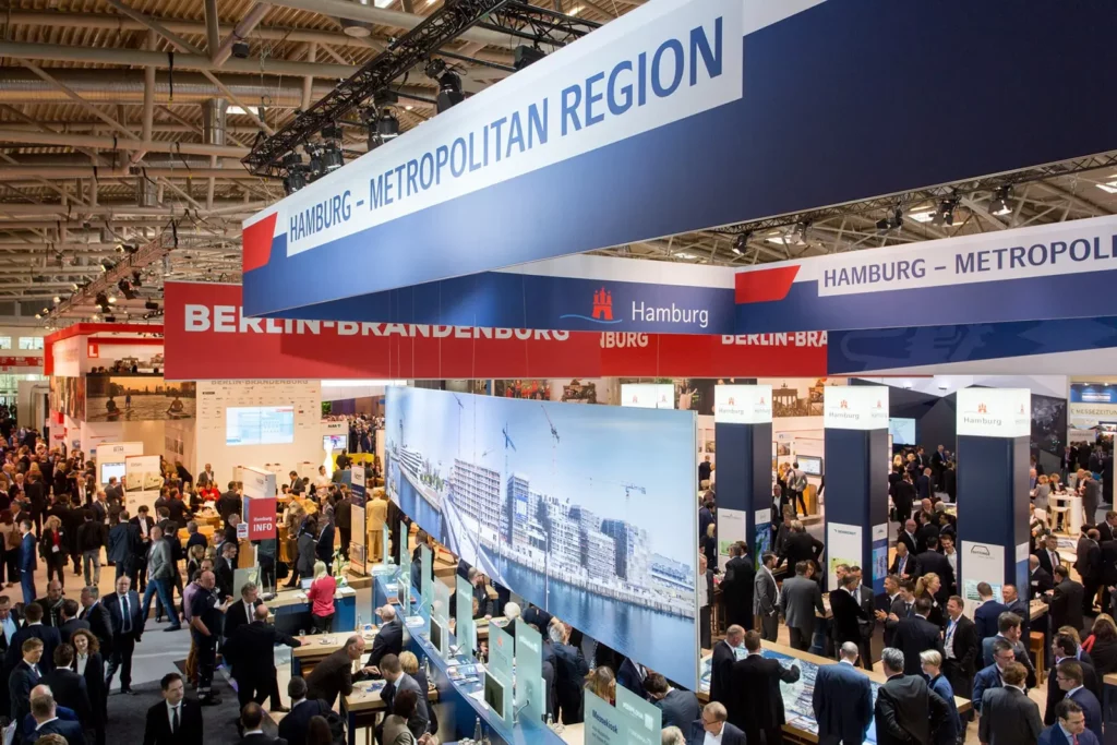 Geschäftsmesse mit Hamburger Stand und zahlreichen Besuchern in großer Ausstellungshalle