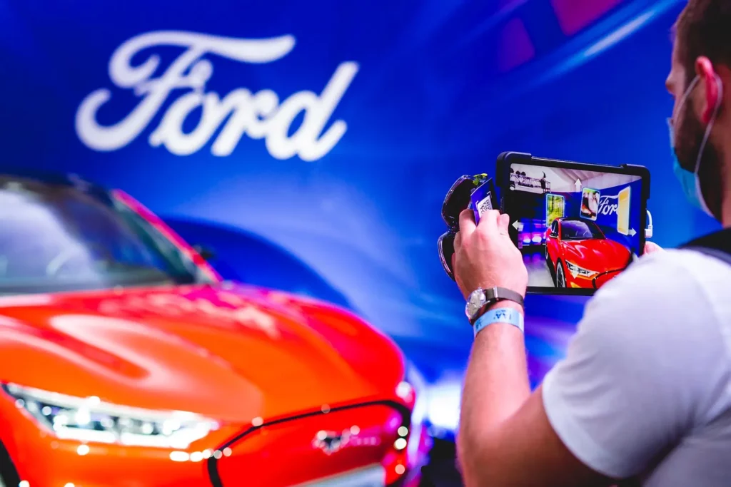Ford-Auto vor blauem Hintergrund, Mann fotografiert mit Smartphone
