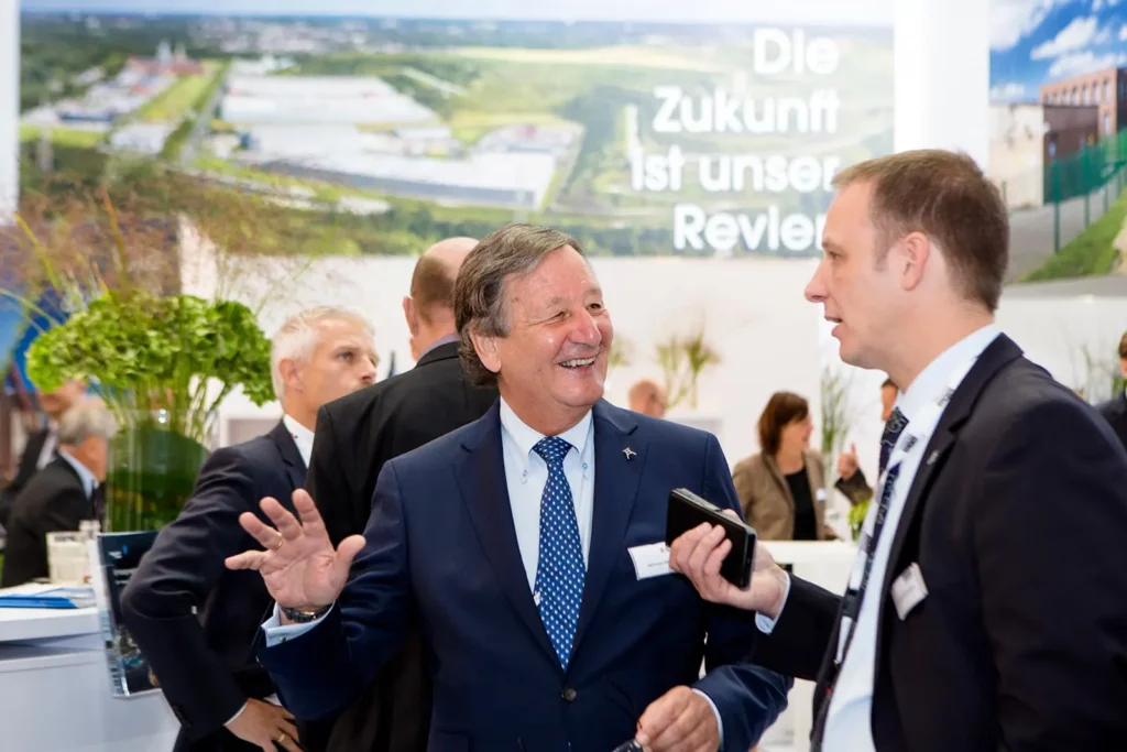 Geschäftsleute im Gespräch auf Messe mit Werbebanner im Hintergrund