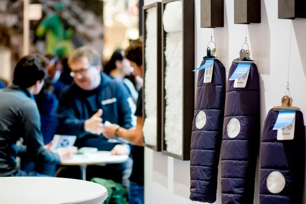 Campingausrüstung auf Messe mit diskutierenden Menschen im Hintergrund