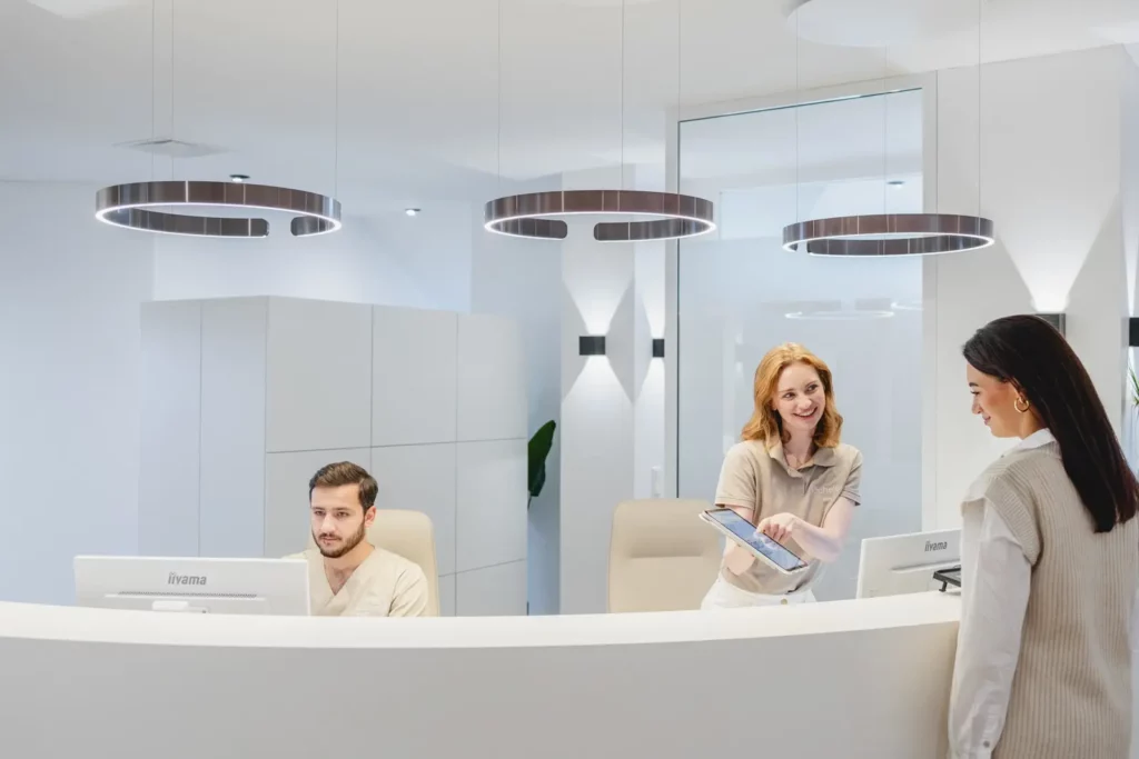 Moderne Arztpraxis mit Empfang, zwei Mitarbeiter begrüßen Patientin