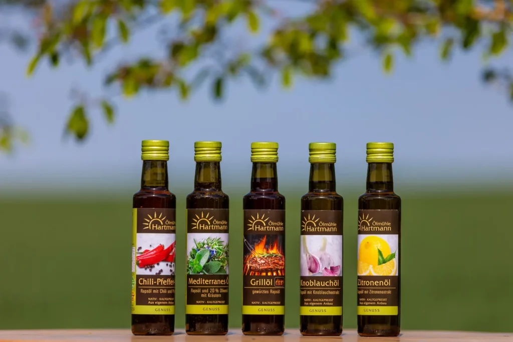 Fünf Olivenölflaschen vor unscharfem Hintergrund, verschiedene Geschmacksrichtungen dargestellt