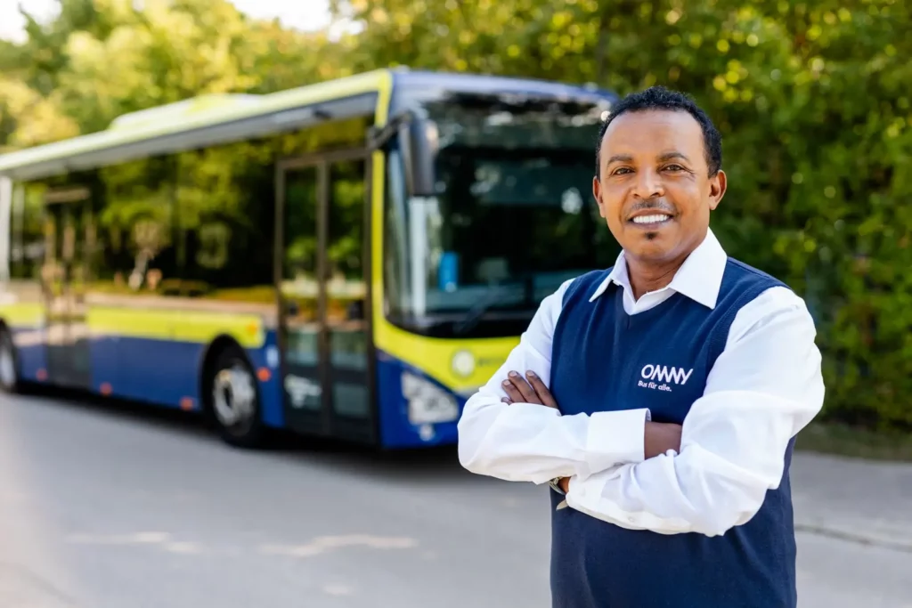 Busfahrer lächelt vor modernem Stadtbus auf ruhiger Straße
