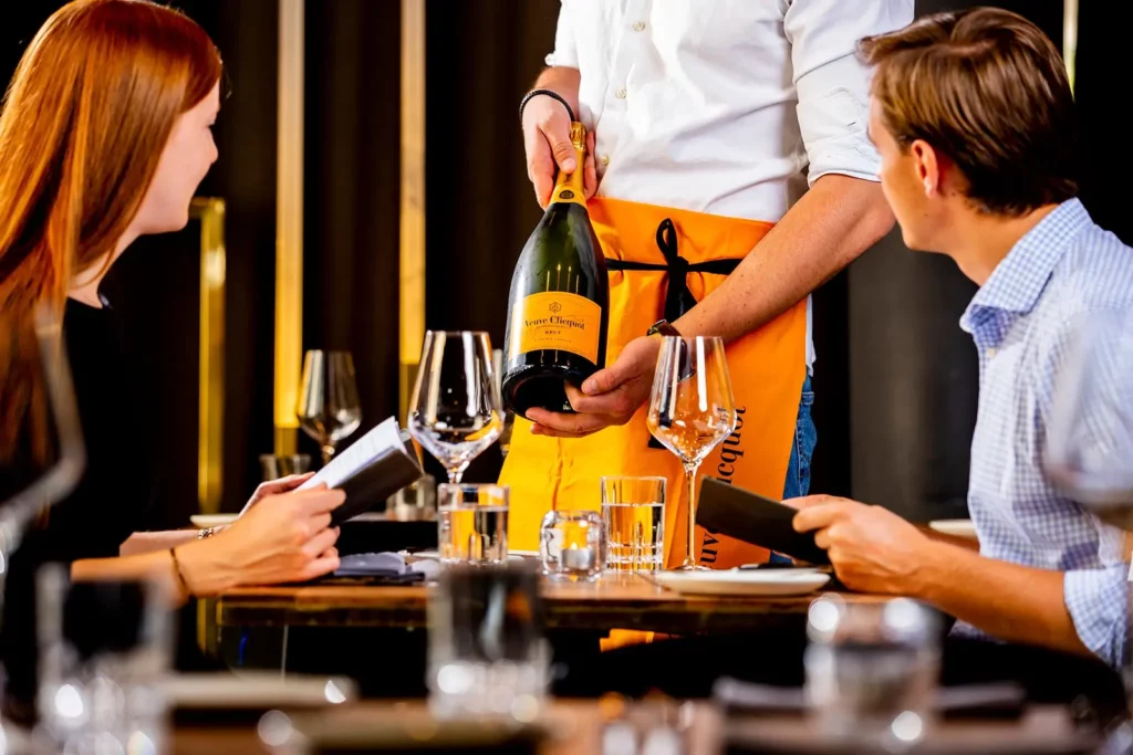 Kellner präsentiert Champagnerflasche an eleganten Tisch mit Gästen