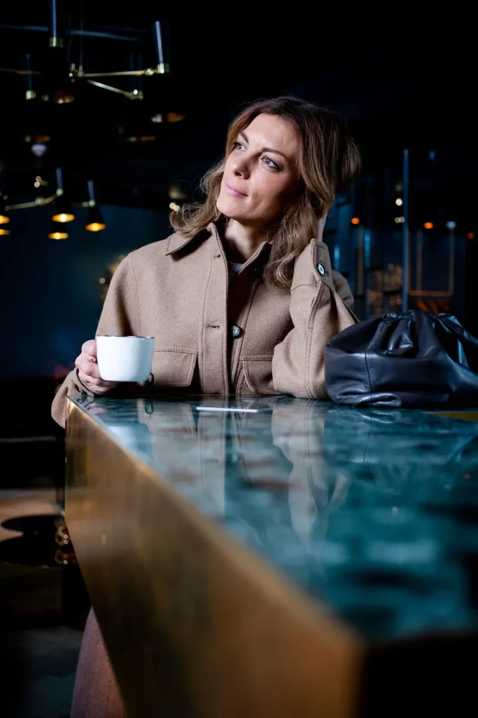 Frau in beige Mantel mit Kaffee an Marmortheke in modernem Café